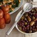 A bowl of olives and a slotted serving spoon on a table in a salad bar.