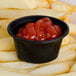 A close up of a black oval plastic souffle cup with ketchup in it.