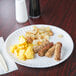 A white 9" uncoated paper plate with breakfast food on a table.