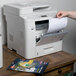 A hand putting Avery High-Visibility Round White Labels into a printer.