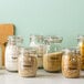 A group of glass jars with Avery clear labels filled with different types of food including granola, oatmeal, and sugar.