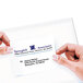 A hand applying a white Avery Repositionable Shipping Label to a business card.