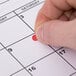 A person's hand using a red Avery Write-On label to mark a calendar date.