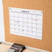 A calendar on a cork board with a red Avery round label on a date.