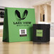 A black box of Avery White Square Labels with a green label on the front next to a green bag with black text.