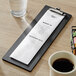 A black wood menu holder with clip on a table with a menu and coffee.