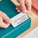 A person's hands holding a piece of paper with Avery White Laser Shipping Labels.
