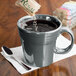 A Fiesta Slate China mug filled with coffee on a counter with a spoon in it.