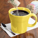 A yellow Fiesta tapered mug on a saucer with liquid being poured into it.