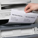 A hand inserting a sheet of Avery White Laser Shipping Labels into a printer.