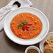 A white Tuxton china bowl of soup with a spoon and a plate of bread.