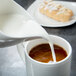 A white Royal Rideau porcelain creamer pouring milk into a cup of coffee.