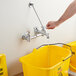 A hand using a Regency wall-mounted mop sink faucet to fill a yellow bucket with water.