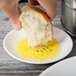 A person holding a piece of bread over a Reserve by Libbey white porcelain dipping dish filled with olive oil.