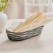 A Tablecraft black wire basket with bread sticks inside.