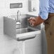 A person washing their hands in a Regency wall-mounted hand sink under a gooseneck faucet with soap.