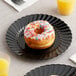 A donut with sprinkles on a WNA Comet black plastic plate next to a glass of orange juice.