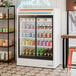 A white refrigerated sliding glass door merchandiser with LED lighting, stocked with various beverages.