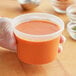 A hand holding a ChoiceHD translucent plastic deli container of orange liquid.