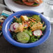 A blue Carlisle Sierrus melamine bowl filled with salad on a counter next to a sandwich and chips.