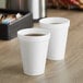 Two Dart white styrofoam cups with liquid on a table.