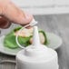 A hand using a white Tablecraft squeeze bottle with a white plastic lid.