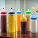 A group of Tablecraft silicone squeeze bottle bands on bottles of different colors and flavors on a table.