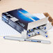 A box of Uni-Ball Vision roller ball pens with blue and white writing on them on a table.