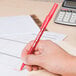 A hand holding a Bic red ballpoint pen over a paper with a calculator.