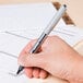 A person using a Uni-ball Vision pen to write on a piece of paper.