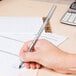 A hand holding a Bic black medium point ballpoint pen writing on a piece of paper.