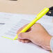 A hand using a Universal Fluorescent Yellow Pen Style Highlighter on a piece of paper.
