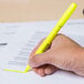 A hand holding a Universal fluorescent yellow pen style highlighter over a paper.