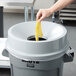 A person holding a banana in a Rubbermaid BRUTE trash can with a funnel top lid.
