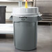 A person cleaning a Rubbermaid trash can with a yellow sponge.