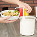 A person pouring salad into a white Cambro cold condiment dispenser with a white lid.