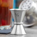 An American Metalcraft stainless steel Japanese style jigger with 0.5 and 0.75 oz. measurements on a table.