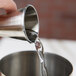 A person using an American Metalcraft stainless steel Japanese style jigger to pour liquid into a cup.