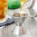 A person using an American Metalcraft stainless steel jigger to pour liquid into a metal cup.