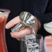 A person using an American Metalcraft stainless steel jigger to pour a cocktail.