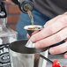 A person using an American Metalcraft stainless steel jigger to pour liquid into a metal cup.