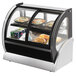 A Vollrath curved countertop display case with food inside.