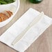 A Visions beige plastic knife on a napkin next to a bowl of food.