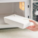 A white microwavable folded paper take-out container being placed into a microwave.