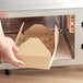 A hand holding a Choice Kraft paper take-out container of food in a microwave.