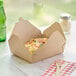 Kraft microwavable folded paper take-out container with food on a table.