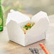 A white Choice paper take-out box filled with food on a table.