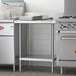 A Regency stainless steel work table with undershelf in a kitchen with a stove.