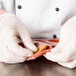 A gloved hand using a Matfer Bourgeat orange silicone tartlet mold to hold a piece of food.