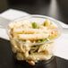 A Fabri-Kal Greenware plastic souffle container of pasta salad on a counter.